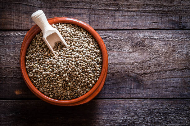 Top view of a brown bowl filled with hemp seeds on a rustic wooden table. A wooden serving scoop is inside the bowl. Predominant color is brown. Low key DSRL studio photo taken with Canon EOS 5D Mk II and Canon EF 100mm f/2.8L Macro IS USM