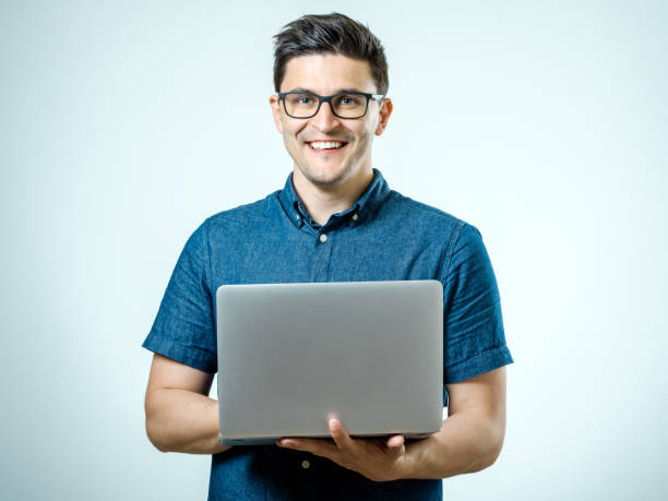 istock Confident young handsome man in shirt holding laptop while standing against white background 835878928