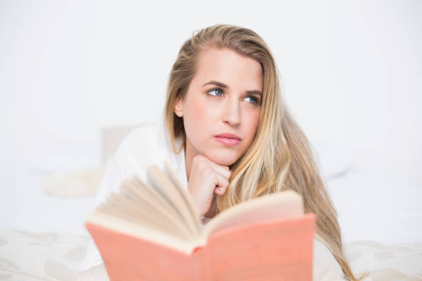 istock Pensive gorgeous model lying on cosy bed holding book 835884962