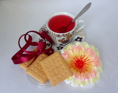 A cup of red Carcade tea and 3 vanila biscuits, decorated with artificial flower, studio shot on white background