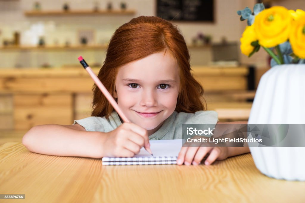 Beautiful Small Redhead Girl Drawing In Notebook And Smiling At Camera