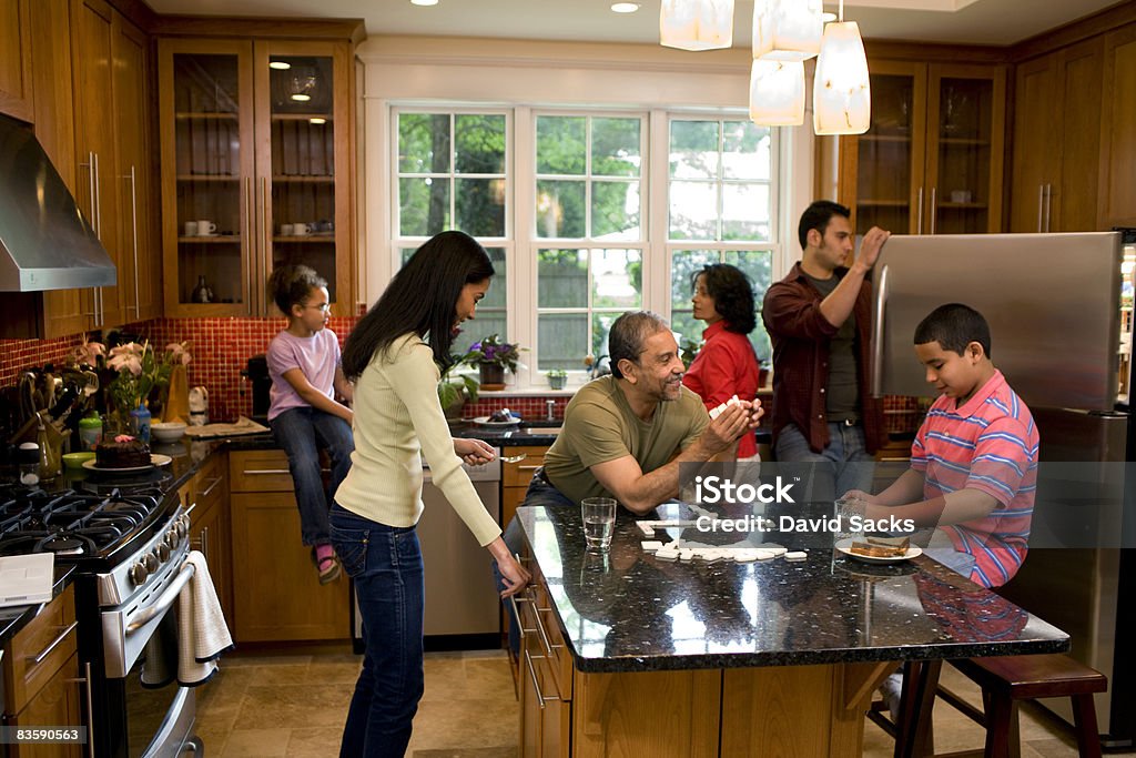 Multigenerational family  in kitchen Grandfather plays dominos with grandson, grandmother talks with granddaughter, mom and dad begin to prepare dinner Family Stock Photo