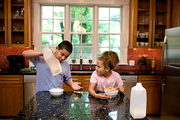 Siblings in kitchen eating breakfast Boy is annoyed because his sister has eaten all the cereal, leaving none for him boys bowl haircut stock pictures, royalty-free photos & images