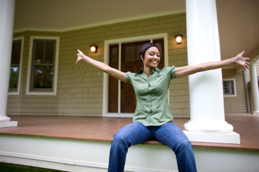 New home owner sitting on porch of suburban home with arms outstretched, showing it off