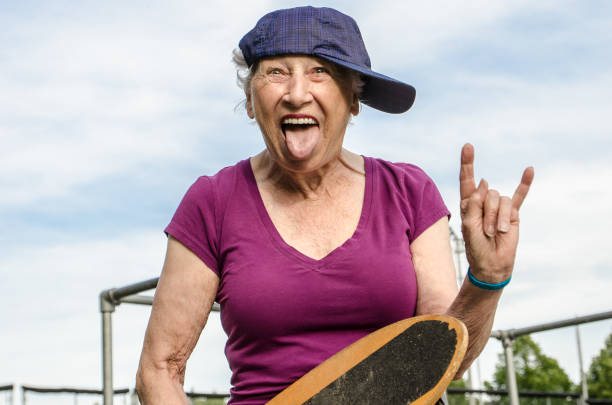 Senior woman with baseball cap on side and holding skateboard while making a face and horn sign during a summer day Senior woman with baseball cap on side and holding skateboard while making a face and horn sign during a summer day woman wearing baseball cap stock pictures, royalty-free photos & images