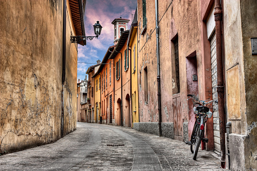 Imola, Bologna, Italy: narrow street at sunset in the old town with bicycle, street lamp, colored houses and bell tower