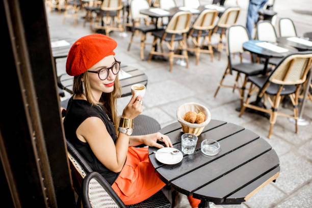 Woman having a french breakfast at the cafe Young stylish woman in red beret having a french breakfast with coffee and croissant sitting oudoors at the cafe terrace beret stock pictures, royalty-free photos & images