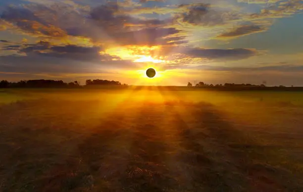 Dramatic sunrise solar Eclipse with sunbeams through clouds over foggy fields.