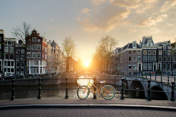 fietsen voering van een brug over de grachten van amsterdam, nederland. fiets is een belangrijke vorm van vervoer in amsterdam, nederland - grachtenpand stockfoto's en -beelden