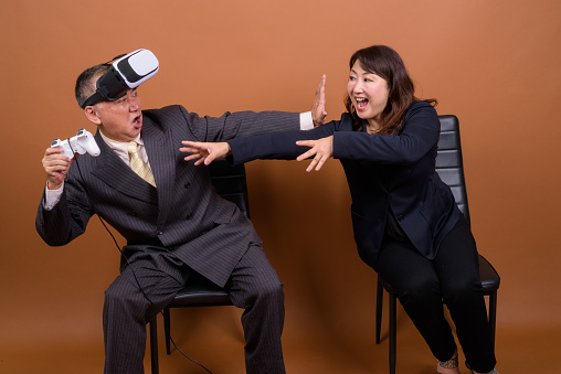 Studio shot of two mature Asian businessman and businesswoman against colored background horizontal shot
