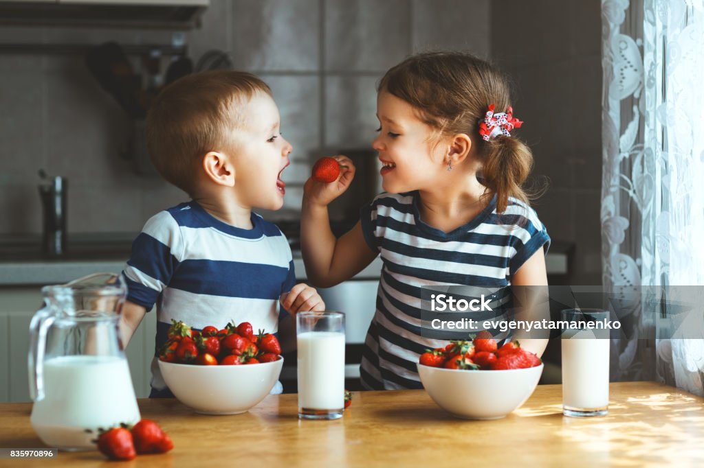 Bambini felici fratello e sorella che mangiano fragole con latte - Foto stock royalty-free di Bambino