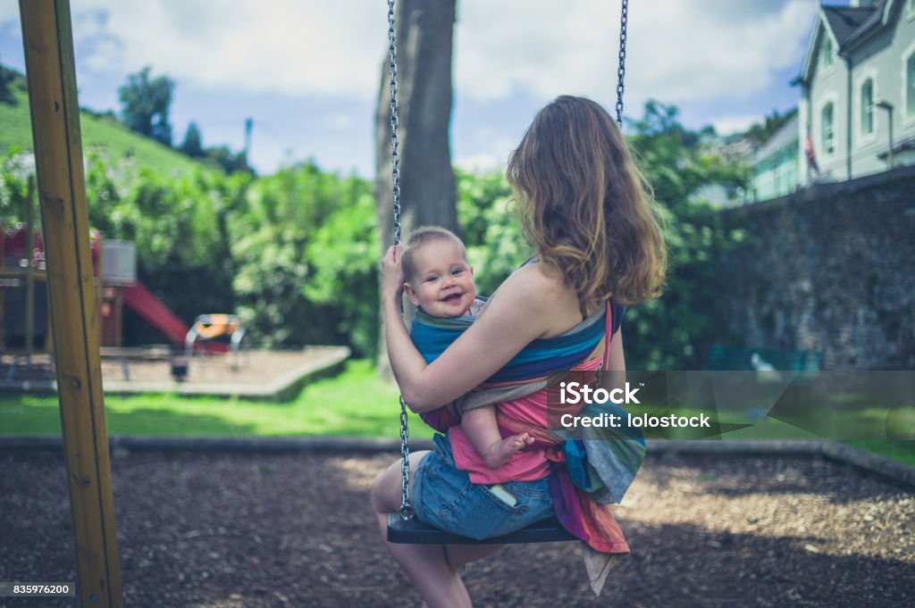 Junge Mutter mit Baby im Tragetuch auf einer Schaukel sitzend - Lizenzfrei Kind Stock-Foto