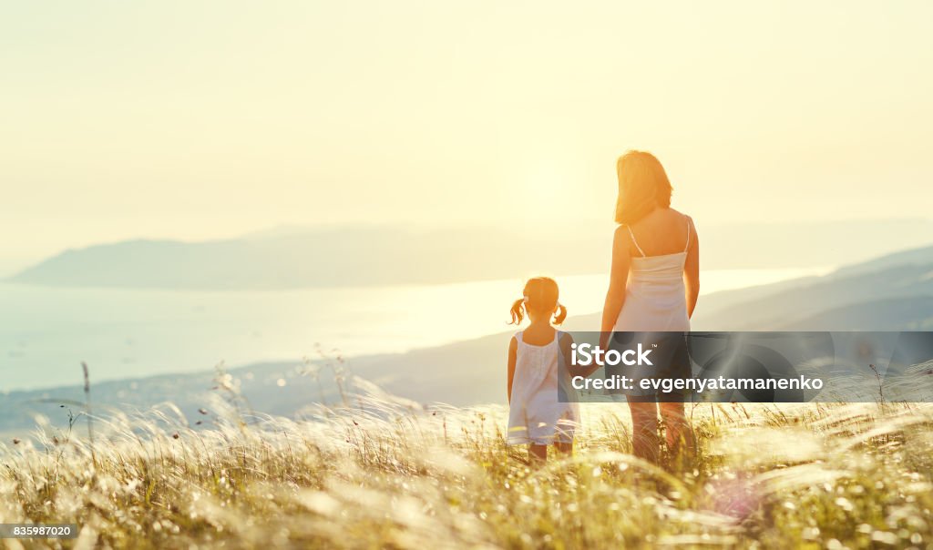 Happy family in summer outdoors. Mother and child daughter stand with their backs on sunset Happy family in summer outdoors. Mother and child daughter stand with their backs and admire sunset Mother Stock Photo