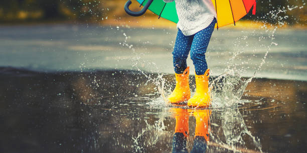 pies de niño en botas de goma amarillas saltando sobre un charco de lluvia - tiempo atmosférico fotos fotografías e imágenes de stock