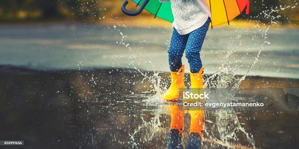 Pieds de l’enfant en caoutchouc jaune bottes sautant par dessus une flaque d’eau sous la pluie - Photo de Enfant libre de droits