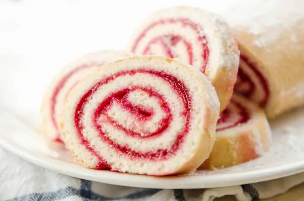 Photo of Fresh sweet roll with strawberry jam and powdered sugar on a plate and white towel