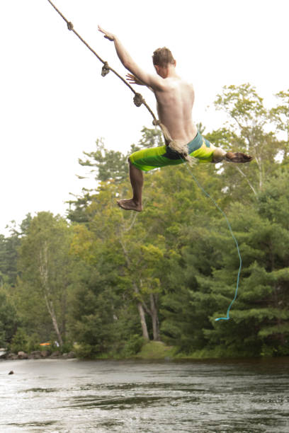 Teenager Flying High On Rope Swing Over Water Stock Photo - Download Image  Now - Rope Swing, Water, Lake - iStock