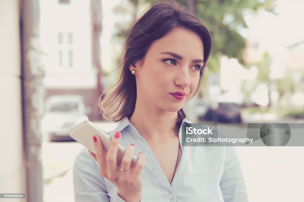 Frustrated annoyed sad woman with mobile phone standing outside in the street with an urban background Irritation Stock Photo