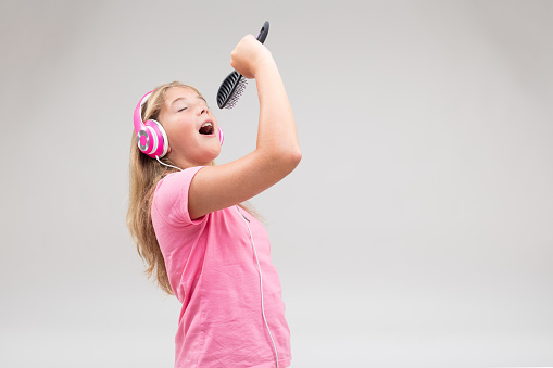 little blonde girl playing as a pop music singer or rock star, pretending and using an hairbrush while she listens to her favourite music in her headphones