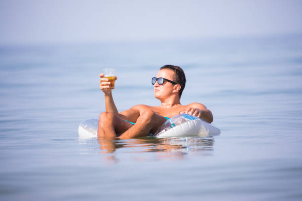 mann in das meerwasser auf kautschuk ring bier trinken und genießen sommer berufung. - swim ring stock-fotos und bilder