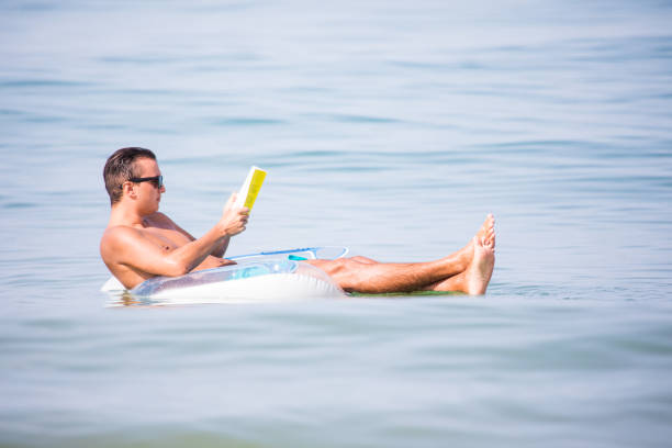 Young man in relax in the ocean water on inflatable ring on sunset read a book. Summer vocation