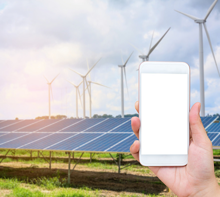 hand holding mobile phone with solar panels and wind turbines background, renewable energy