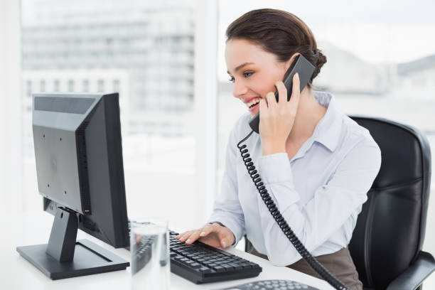 istock Smiling businesswoman using landline phone and computer in office 836070232