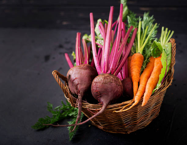 Young beetroot and carrots with a tops in a basket on a dark background.