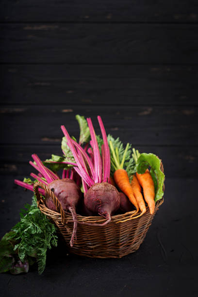 Young beetroot and carrots with a tops in a basket on a dark background.