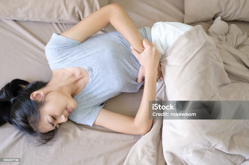 Junge schöne Frau mit langem Haar Curl up auf dem braunen Bett mit Magen Schmerzen schlafen, weil Menstruationsschmerzen Soft Fokus Hintergrund - Lizenzfrei Bauch Stock-Foto