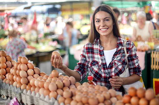 Young beautiful woman choosing eggs at a farmer's market. About 25 years old, smiling Caucasian brunette.