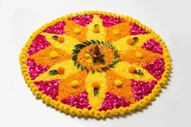 flower rangoli for Diwali or pongal made using marigold or zendu flowers and red rose petals over white background with diwali diya in the middle, selective focus