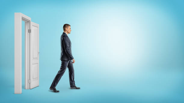 A businessman on blue background walking through an open white doorframe A businessman on blue background walking through an open white doorframe. New business ventures. Entering new market. Career growth. side view stock pictures, royalty-free photos & images