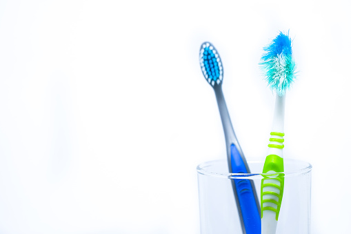 New toothbrush and old toothbrush (damaged) in clear glass for teeth cleaning isolated on white background - concept 