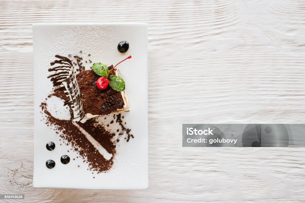 Tiramisu on white plate with decoration Tiramisu on white plate with decoration from chocolate,  cherry and mint. Sweet dessert serving in restaurant, free space nearby, top view Dessert - Sweet Food Stock Photo
