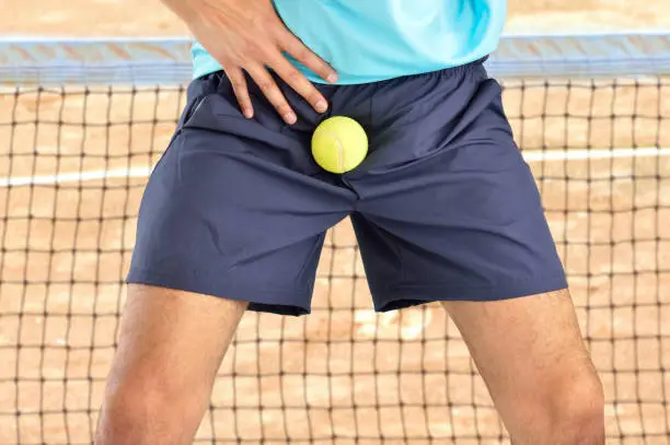 man playing tennis being hit by a tennis ball with force in the crotch when he misses a catch or as an unexpected accident on a clay court