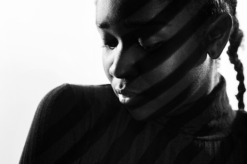 Creative diagonal stripes from projection light on beautiful woman with dark skin. Black and white studio portrait.