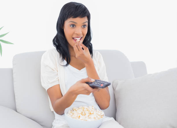 istock Focused black haired woman in white clothes watching tv while eating popcorn 836167042