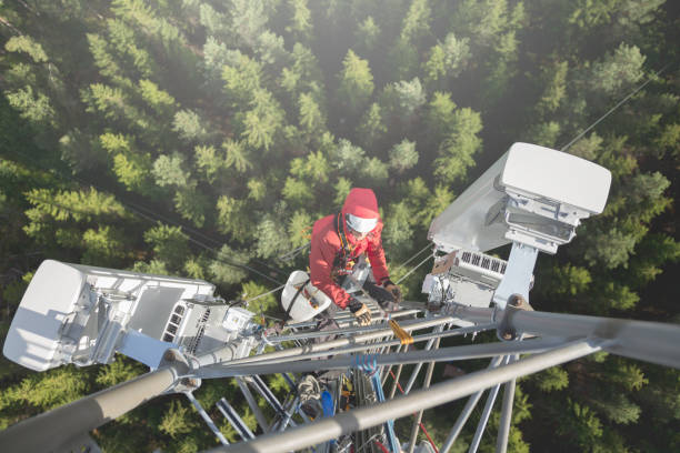 Working at height Telecommunication manual high worker engineer installing new 3g 4g LTE antenna on tall mobile base station (communication tower) in the middle of european forest, high angle of view. Working at height. Telecommunication masts and towers are typically tall structures designed to support antennas for telecommunications and broadcasting. Drone point of view. telecommunications equipment stock pictures, royalty-free photos & images