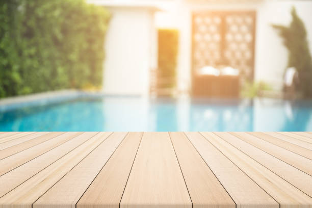 Empty wooden table in front with blurred background of swimming pool stock photo