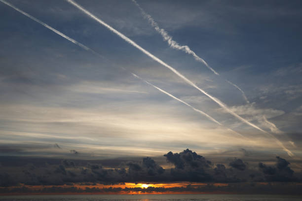 View of the sunset over the sea with dark clouds and white lines in the sky