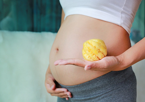 Pregnant woman holding pineapple at her belly. Dieting Concept. Healthy Lifestyle.