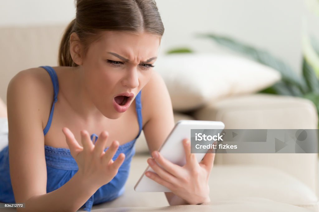 Shocked young woman using digital tablet at home Young woman feeling shocked and looking with confusion on digital tablet screen while browsing online at home. Outrageous photos or disgusting content in social network, unbelievable news in Internet Disgust Stock Photo