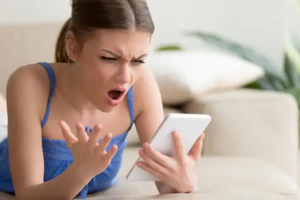 Young woman feeling shocked and looking with confusion on digital tablet screen while browsing online at home. Outrageous photos or disgusting content in social network, unbelievable news in Internet