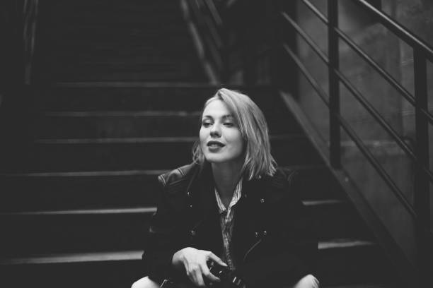 Black and white photo of a beautiful woman sitting on the steps and holding camera and photographing