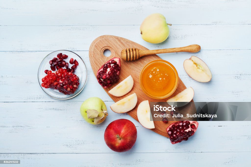 Table set with traditional food for Jewish New Year Holiday, Rosh Hashana. Honey, apple slices and pomegranate. Flat lay. Honey, apple slices and pomegranate serve on kitchen board top view. Table set with traditional food for Jewish New Year Holiday, Rosh Hashana. Rosh Hashanah Stock Photo
