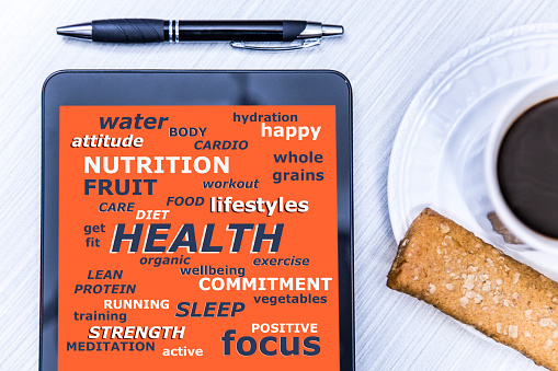 Health word cloud on orange digital tablet screen with coffee in white mug, health bar, and pen on desk.