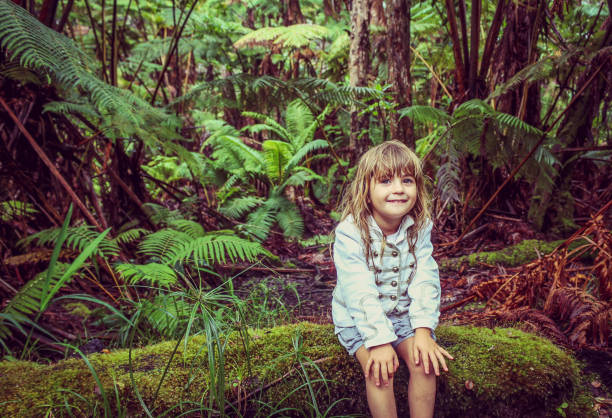 eight-year-old girl in a red swimsuit sitting on the rocks at the edge of a crystal clear river smiling at the camera