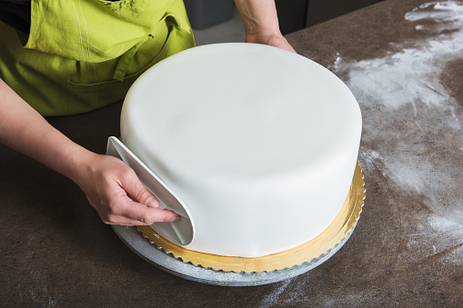 Mujer irreconocible en panadería decorando la tarta con fondant blanco photo