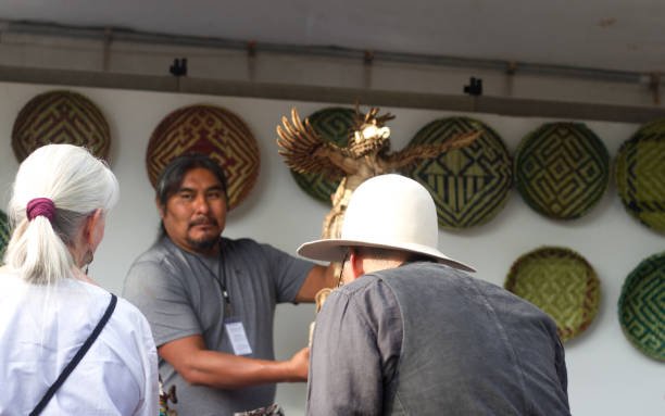 2017 Santa Fe Indian Market: Hopi Sculptor with Kachina Dolls Santa Fe, NM, USA: Hopi artist Arthur Holmes showing his carved Kachina dolls to tourists at the 2017 Santa Fe Indian Market. The market, now in its 96th year, is spread out around the historic Santa Fe Plaza, showcasing North American Indigenous arts and culture. More than 900 artists from hundreds of tribes participate in the two-day event; visitors number about 100,000. kachina doll stock pictures, royalty-free photos & images